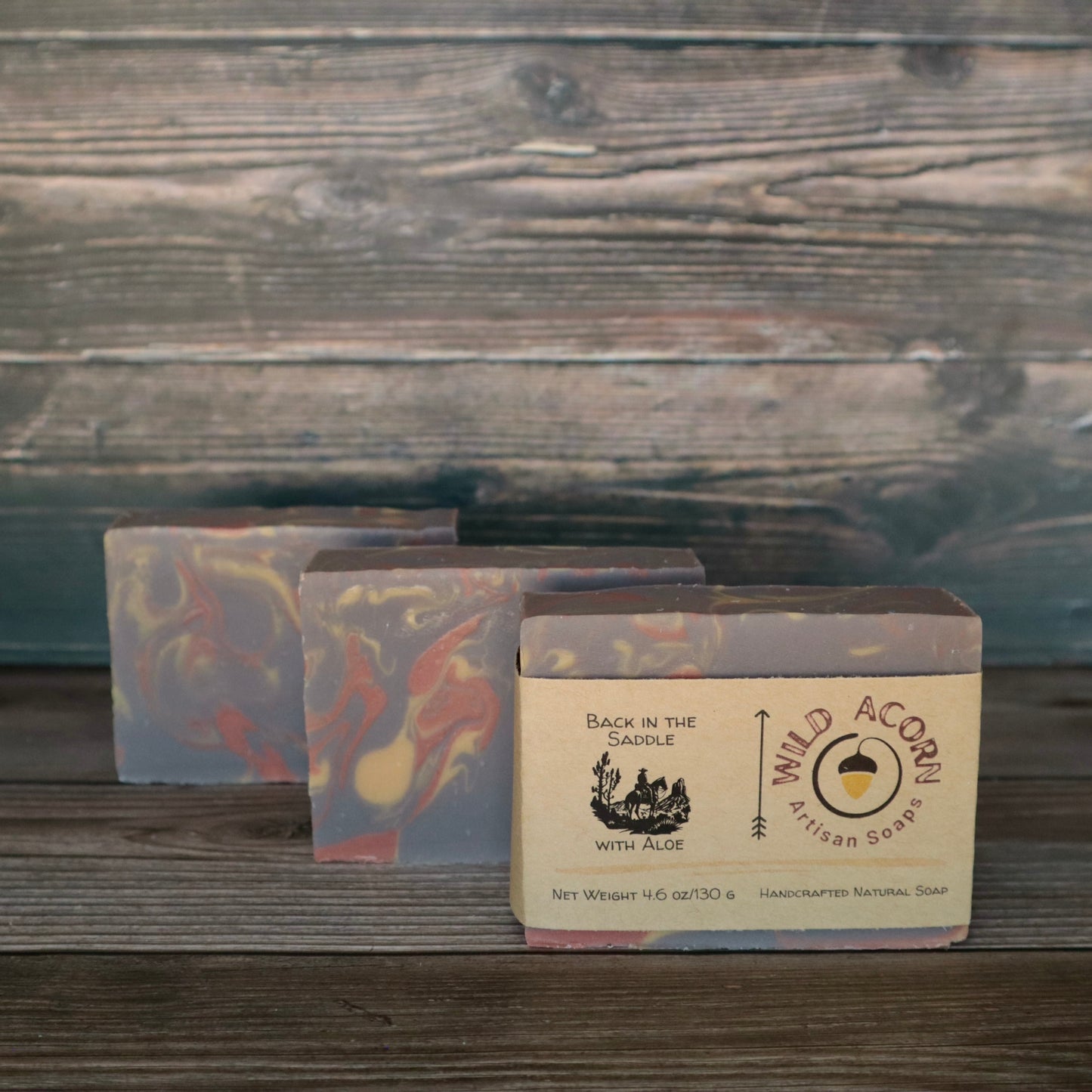Three bars of soap with orange/red, brown, and cream colored swirls. One bar has a label on it with a picture of a man riding a horse.