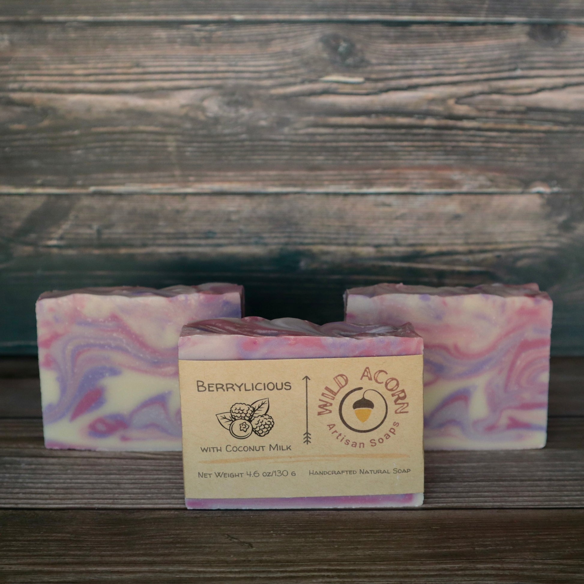 Three bars of soap colored pink, purple and white swirled together to represent berry colors. One bar has a label on it with a picture of two raspberries and a blueberry and two leaves.