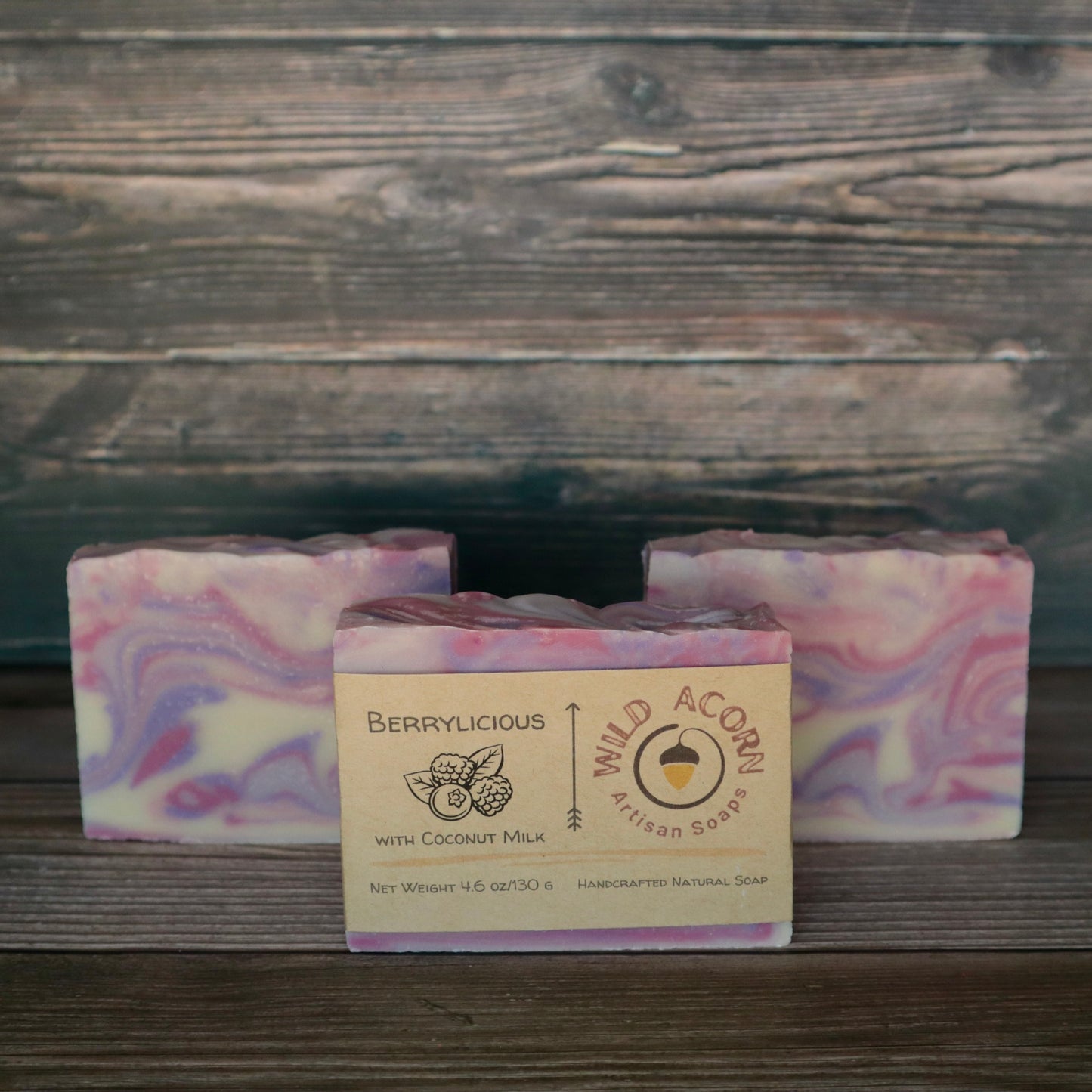 Three bars of soap colored pink, purple and white swirled together to represent berry colors. One bar has a label on it with a picture of two raspberries and a blueberry and two leaves.