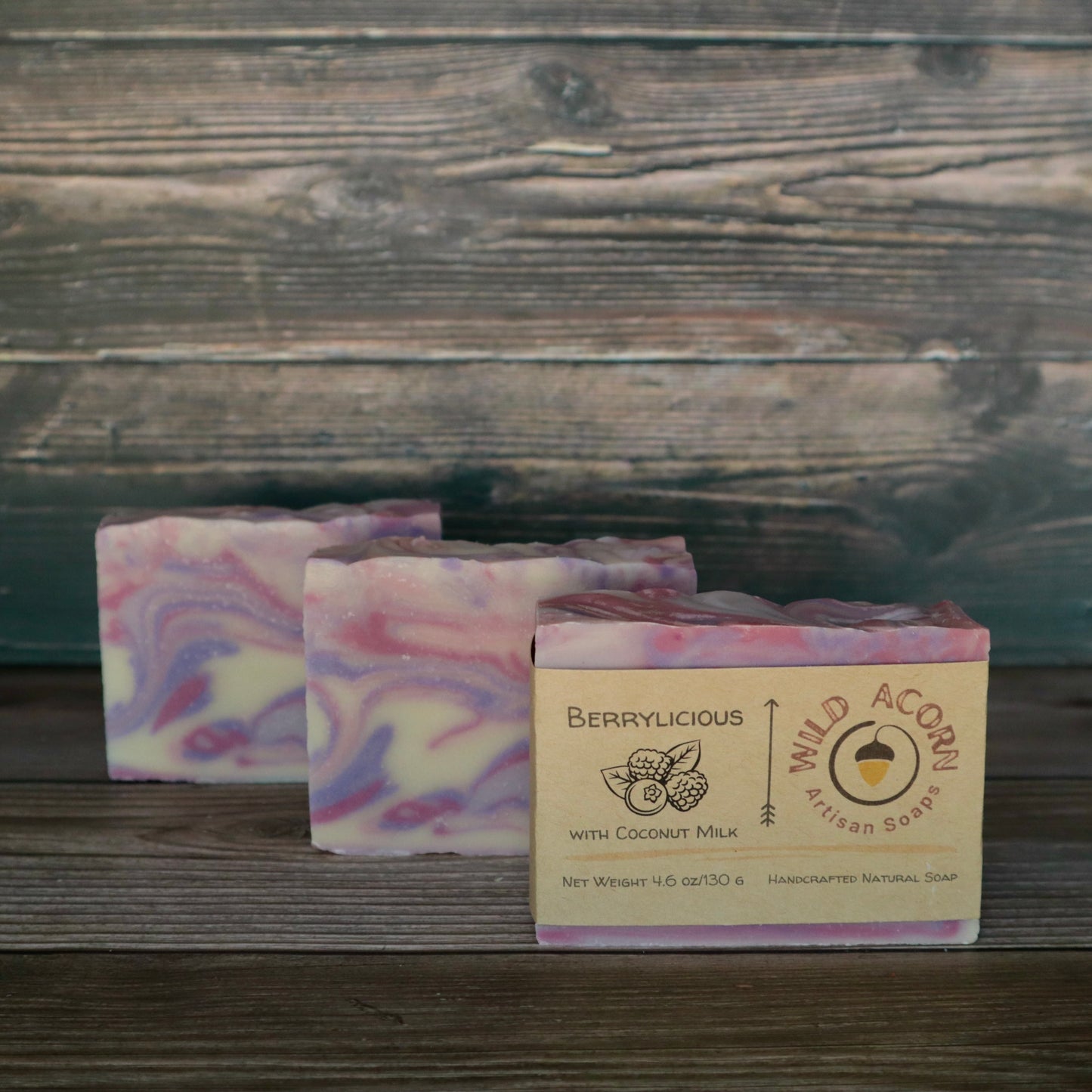 Three bars of soap colored pink, purple and white swirled together to represent berry colors. One bar has a label on it with a picture of two raspberries and a blueberry and two leaves.