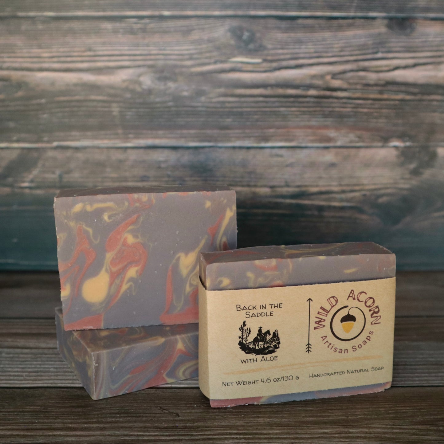 Three bars of soap with orange/red, brown, and cream colored swirls. One bar has a label on it with a picture of a man riding a horse.