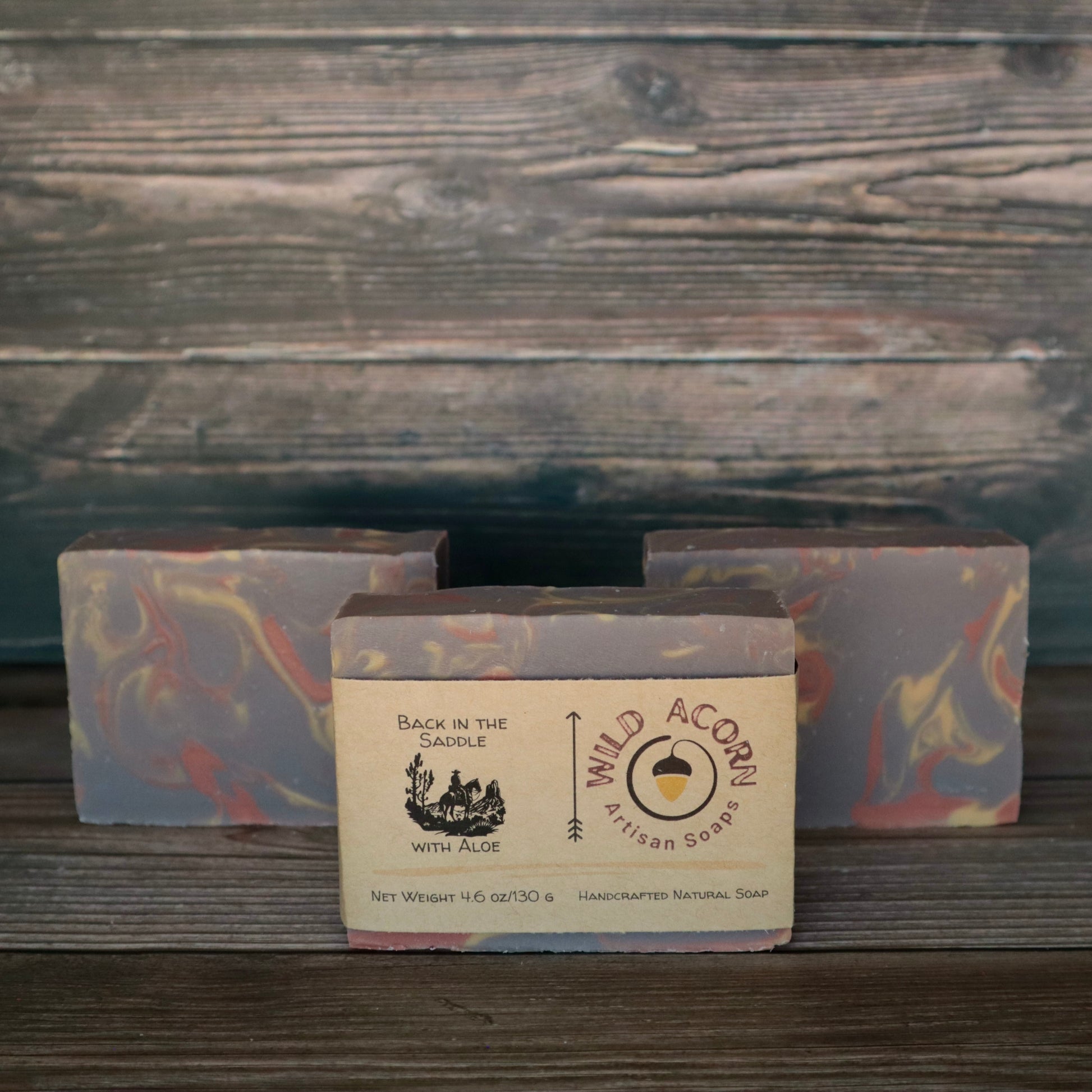 Three bars of soap with orange/red, brown, and cream colored swirls. One bar has a label on it with a picture of a man riding a horse.