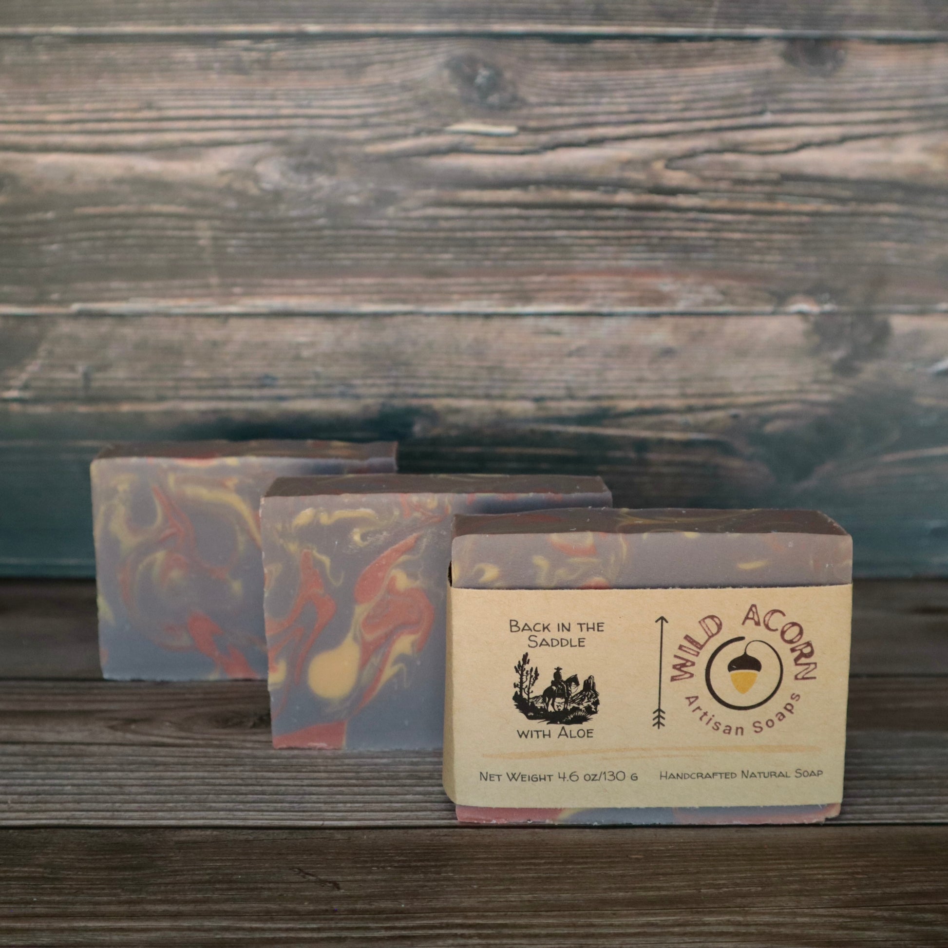 Three bars of soap with orange/red, brown, and cream colored swirls. One bar has a label on it with a picture of a man riding a horse.