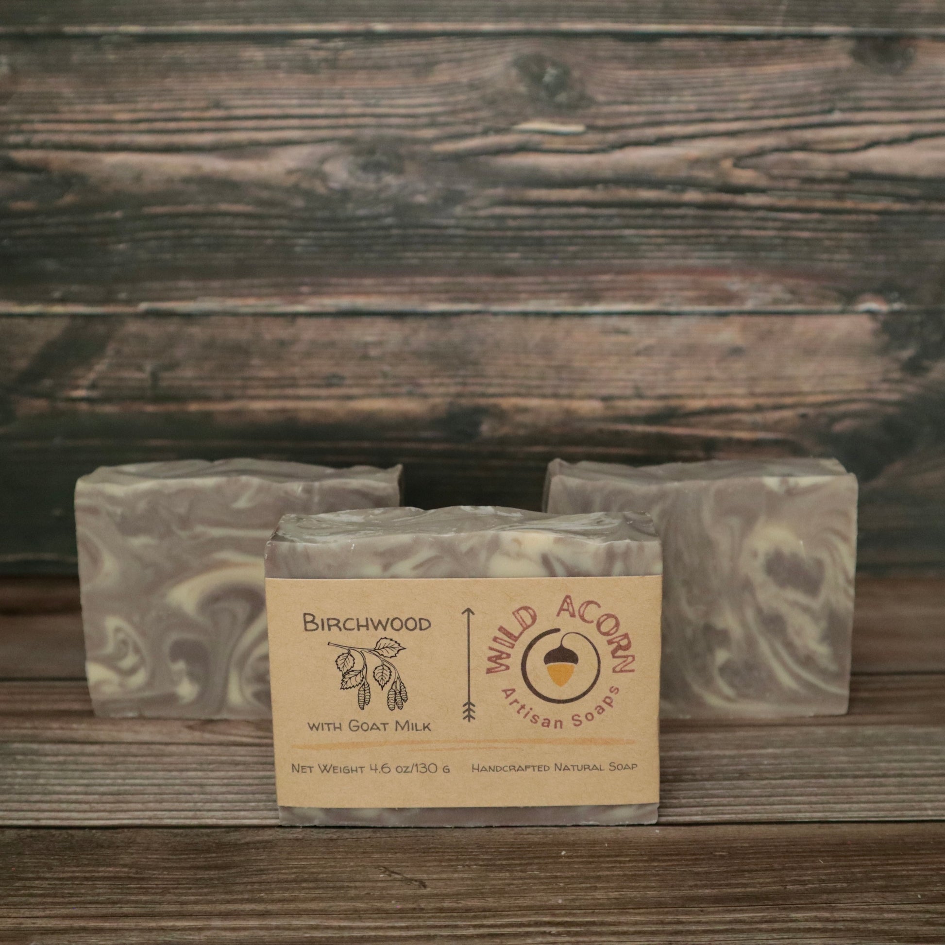 Three bars of soap with light brown and white/cream swirls resembling wood grain. One bar has a label on it with a picture of a branch from a birch tree that has leaves and seed pods hanging down.