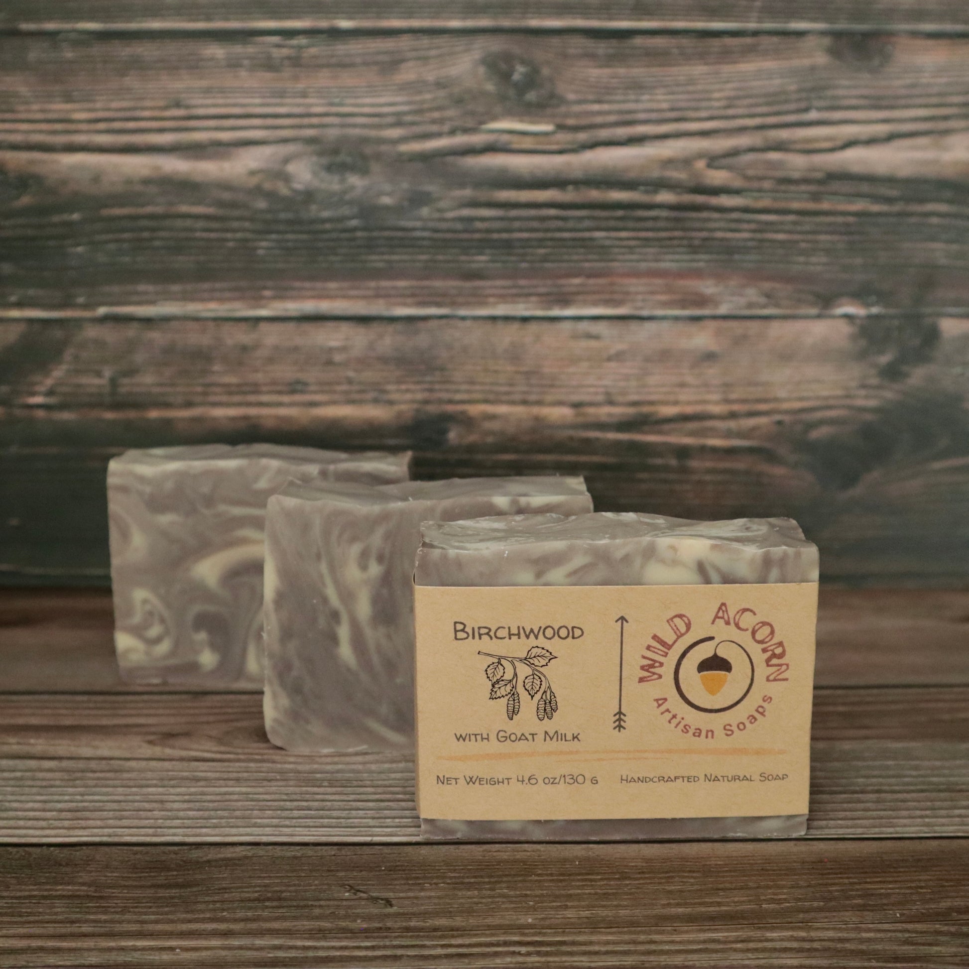 Three bars of soap with light brown and white/cream swirls resembling wood grain. One bar has a label on it with a picture of a branch from a birch tree that has leaves and seed pods hanging down.