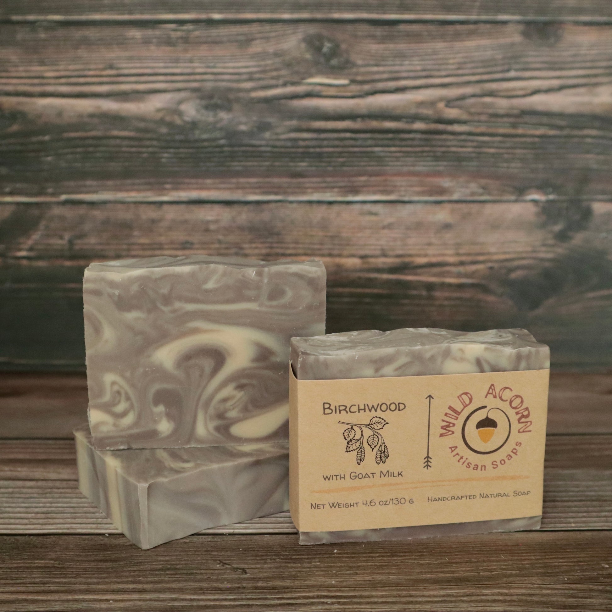 Three bars of soap with light brown and white/cream swirls resembling wood grain. One bar has a label on it with a picture of a branch from a birch tree that has leaves and seed pods hanging down.