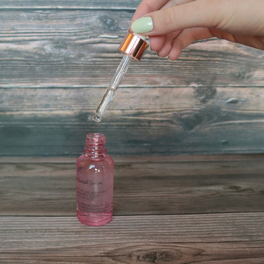 hand holding the dropper lid portion of the bottle above a pink dropper bottle to show the dropper tube.e